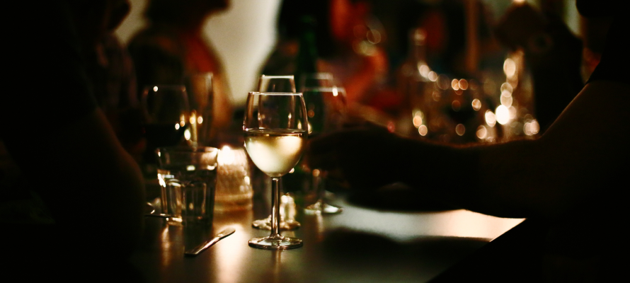 A dimly lit restaurant and a glass of white wine in the foreground